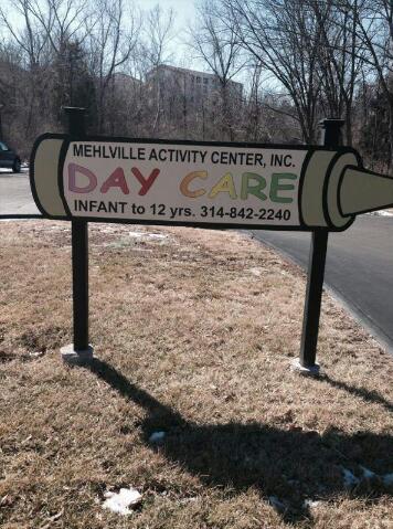 Mehlville Activity Center sign, positioned on a small patch of grass in front of the building, near the parking lot.
