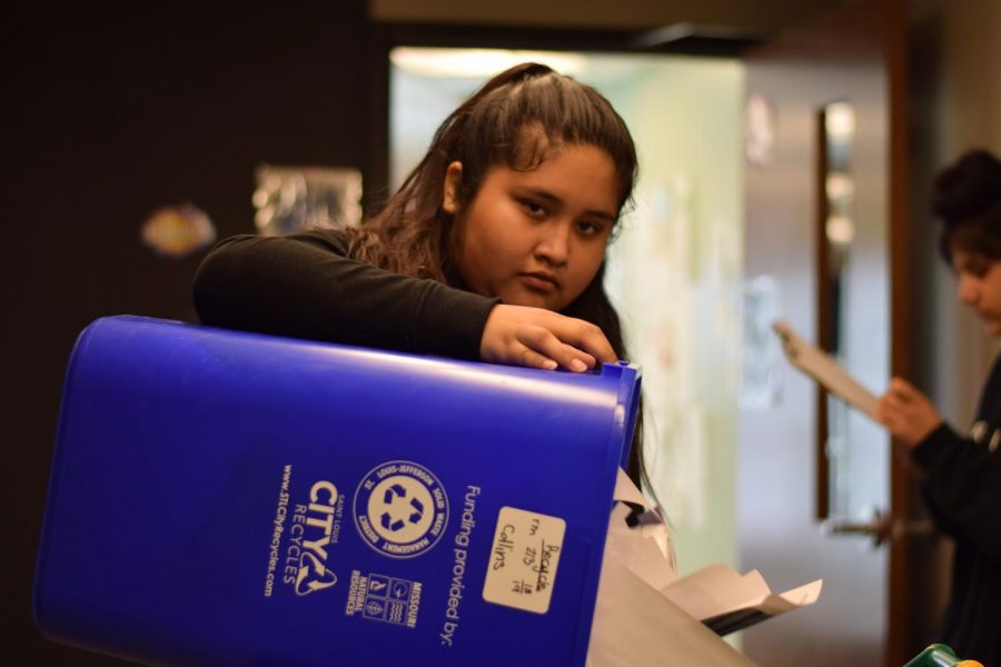 Seventh grader Aelilian Ceron-Reyes dumps waste from a classroom recycling bin into the main recycling can.