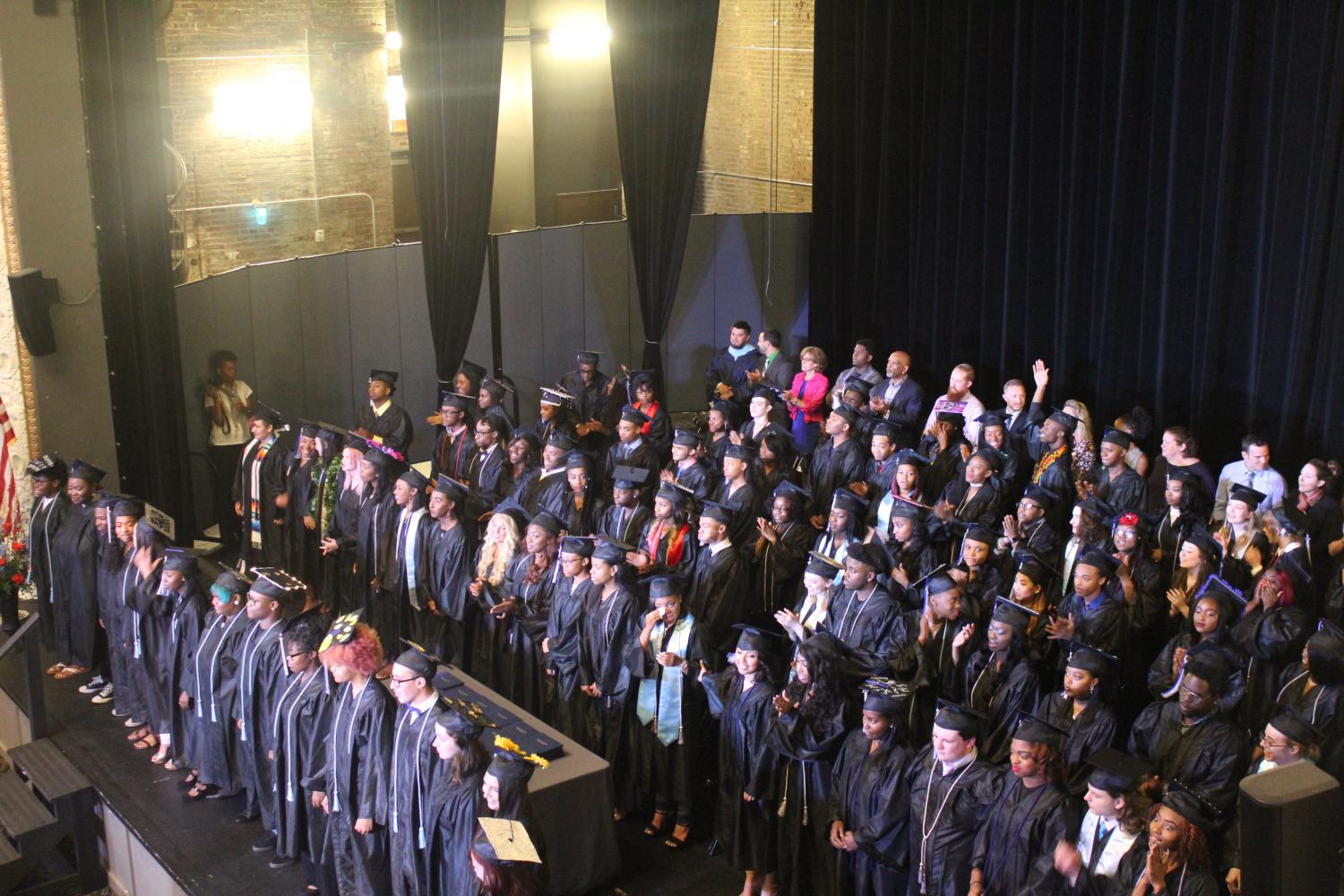 The class of 2017 stands on the stage, waiting for the National Anthem to be sung by choir students, standing in front. 