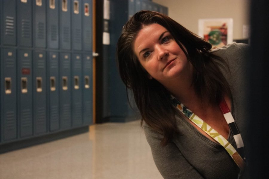Laura Schuhwerk, Makerspace poses for a photo illustration of her conducting a hall sweep and finding a student hiding in between two sets of lockers.  Hall sweeps are conducted by teachers on their plan period.