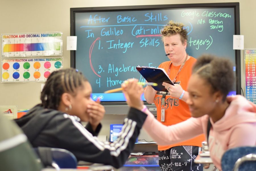 Photo illustration.  7th grader India Mitchell and 7th grader Janelle Briggs horseplay in math class as 7th Grade Math teacher writes them up for minors on her clipboard.